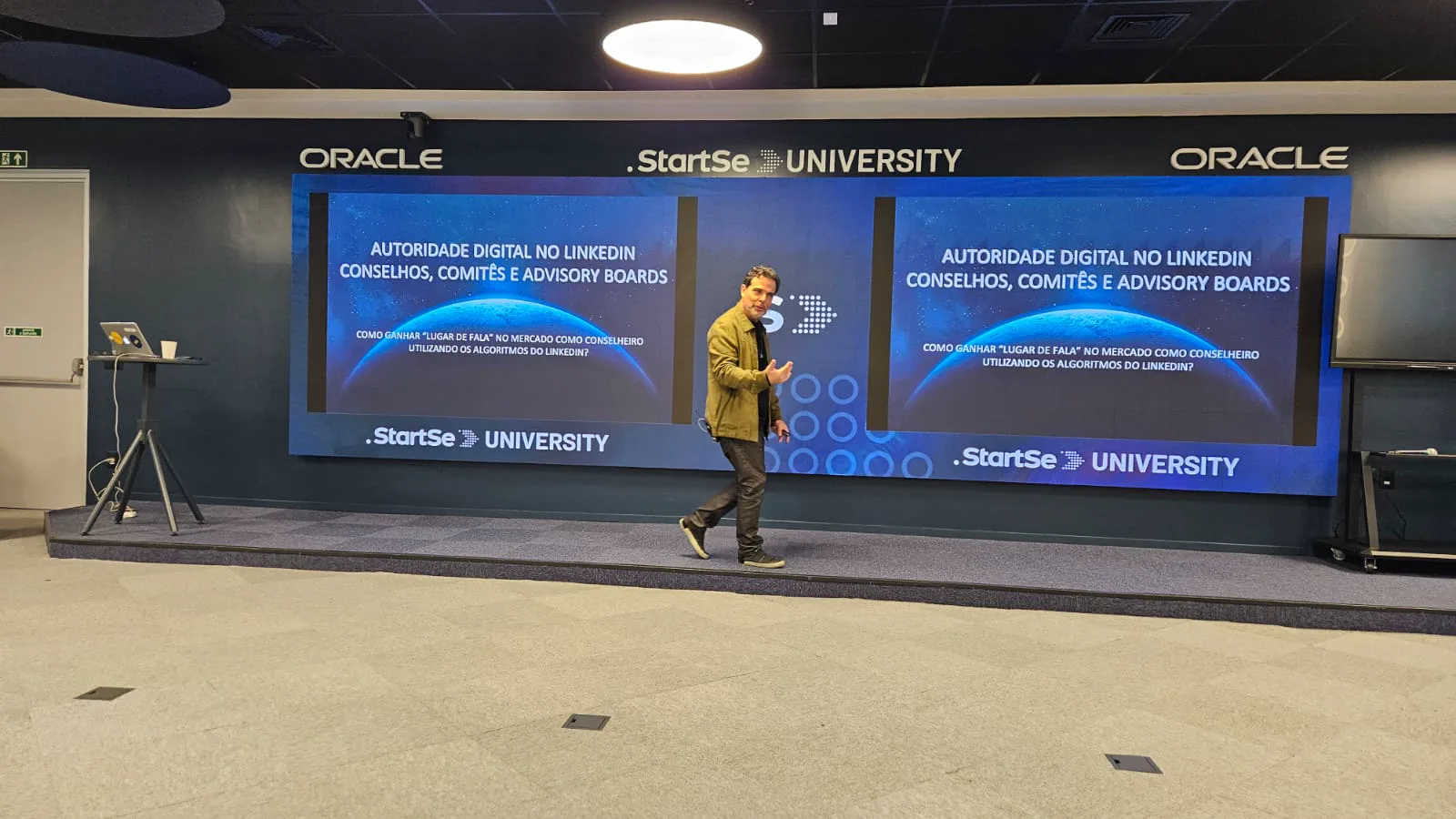 Prof Calixto caminhando no palco diante de dois painéis de LED com o tema autoridade digital no LinkedIn para conselhos, comitês e advisory boards.